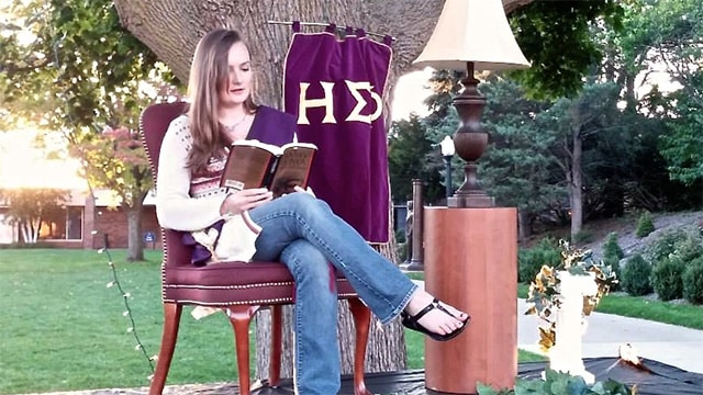 Student sitting outside with with a rug and table lamp reading.